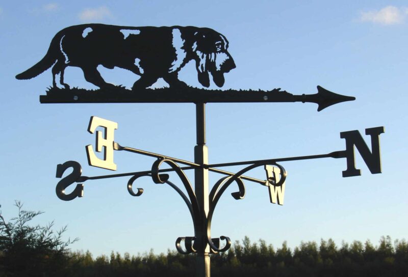 a black Basset Hound Dog Weathervane against a blue sky and hedge row