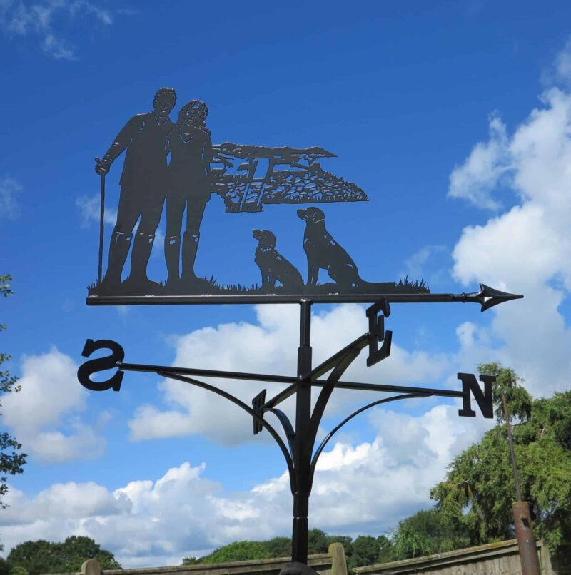 a dog walker themed weathervane, picturing a Couple Walking, Hills And Dogs against a blue sky