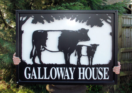 Belted Galloways farm sign with white backing sheet against dark backdrop